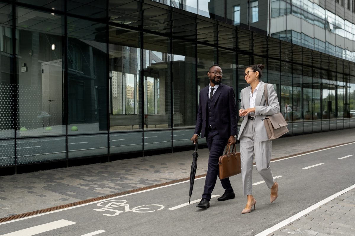 Two happy young intercultural colleagues walking down modern street